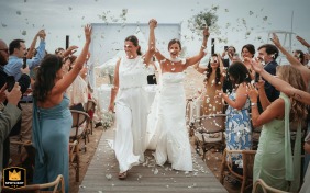 At Armazem do Sushi in Lavra, North of Portugal, the newly married brides walk hand in hand from their beach ceremony toward the venue, radiating happiness as they begin their celebration surrounded by cheering guests.
